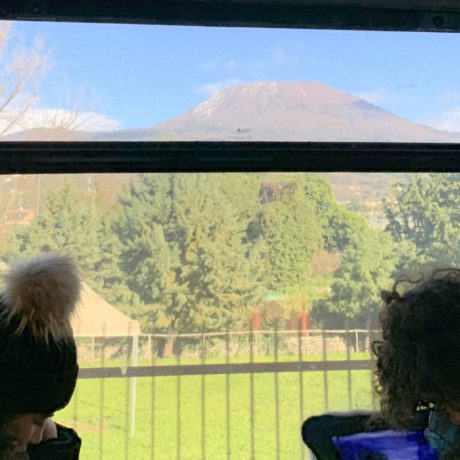 Pessoas em um trem na Europa olhando a janela e vendo o Monte Vesúvio