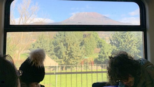 Pessoas em um trem na Europa olhando a janela e vendo o Monte Vesúvio